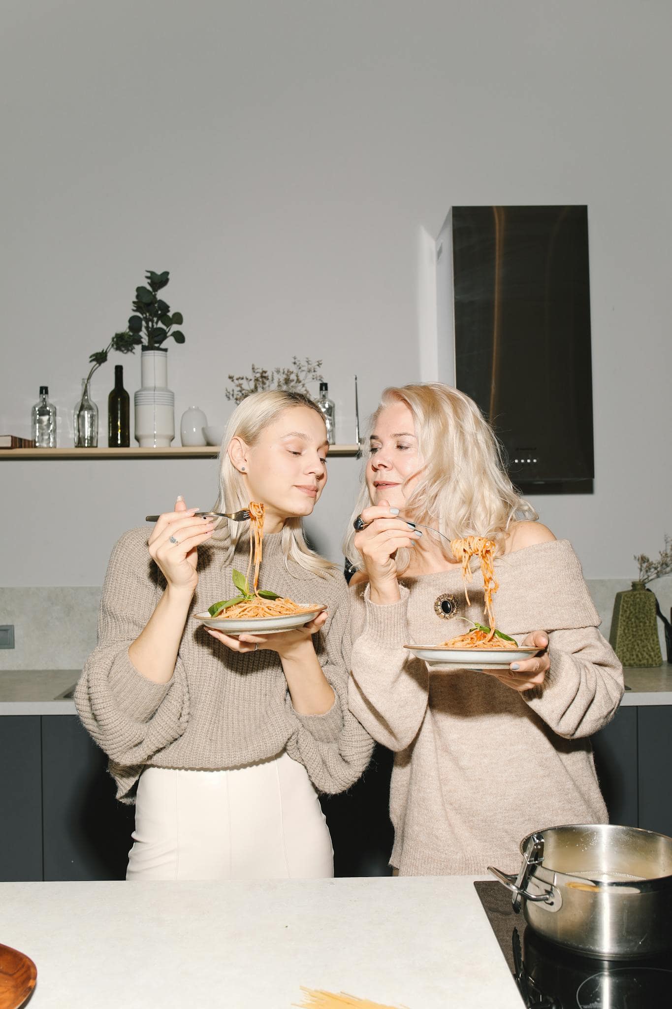 Home A Joyful Blonde Mother And Daughter Enjoying Pasta In The Kitchen Showcasing Family Bonding And Italian Cuisine. 6073641 1365x2048